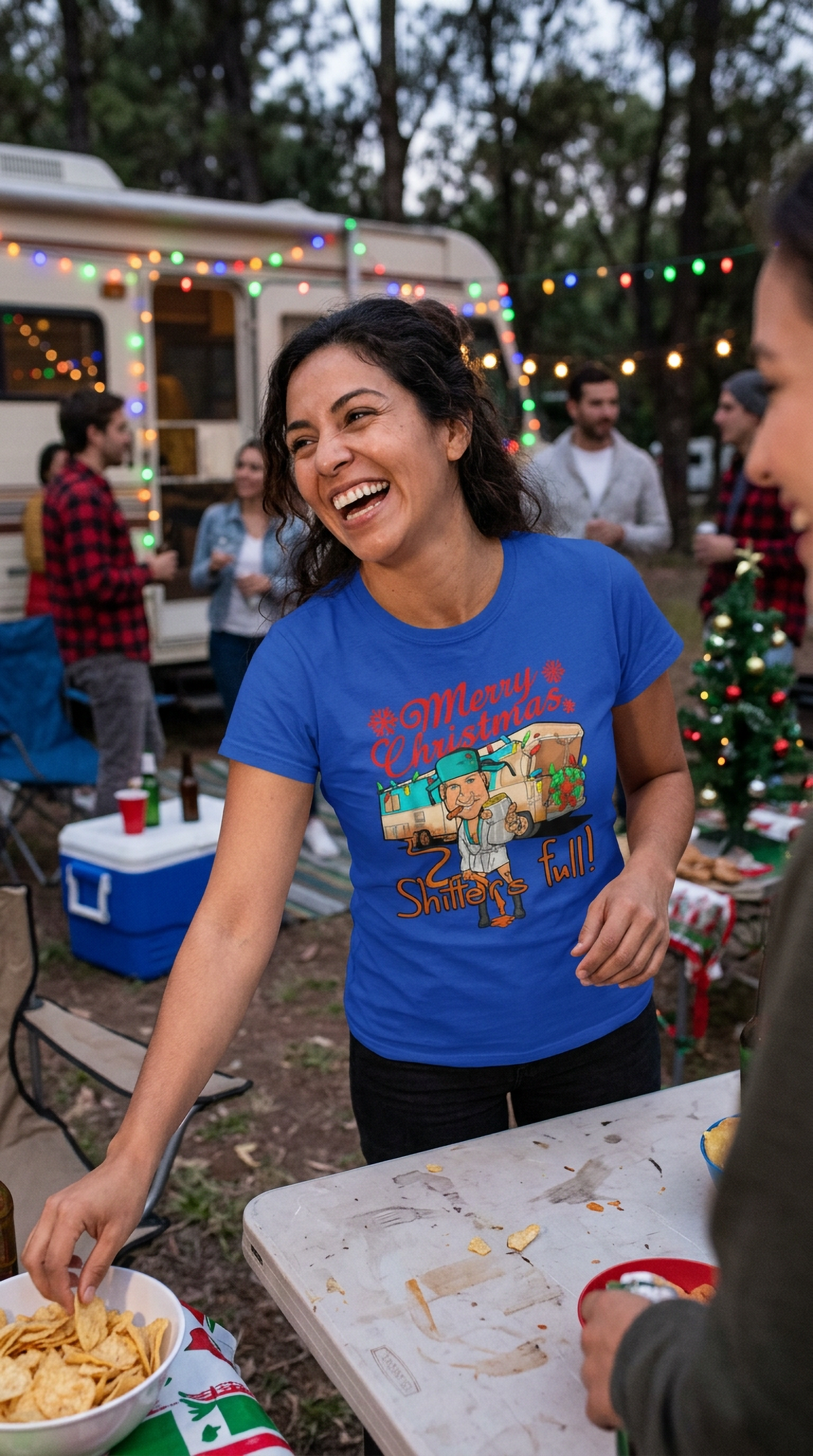 Lifestyle – Blue: Woman wearing a blue funny Christmas graphic t-shirt with festive camper artwork at an outdoor holiday event.
