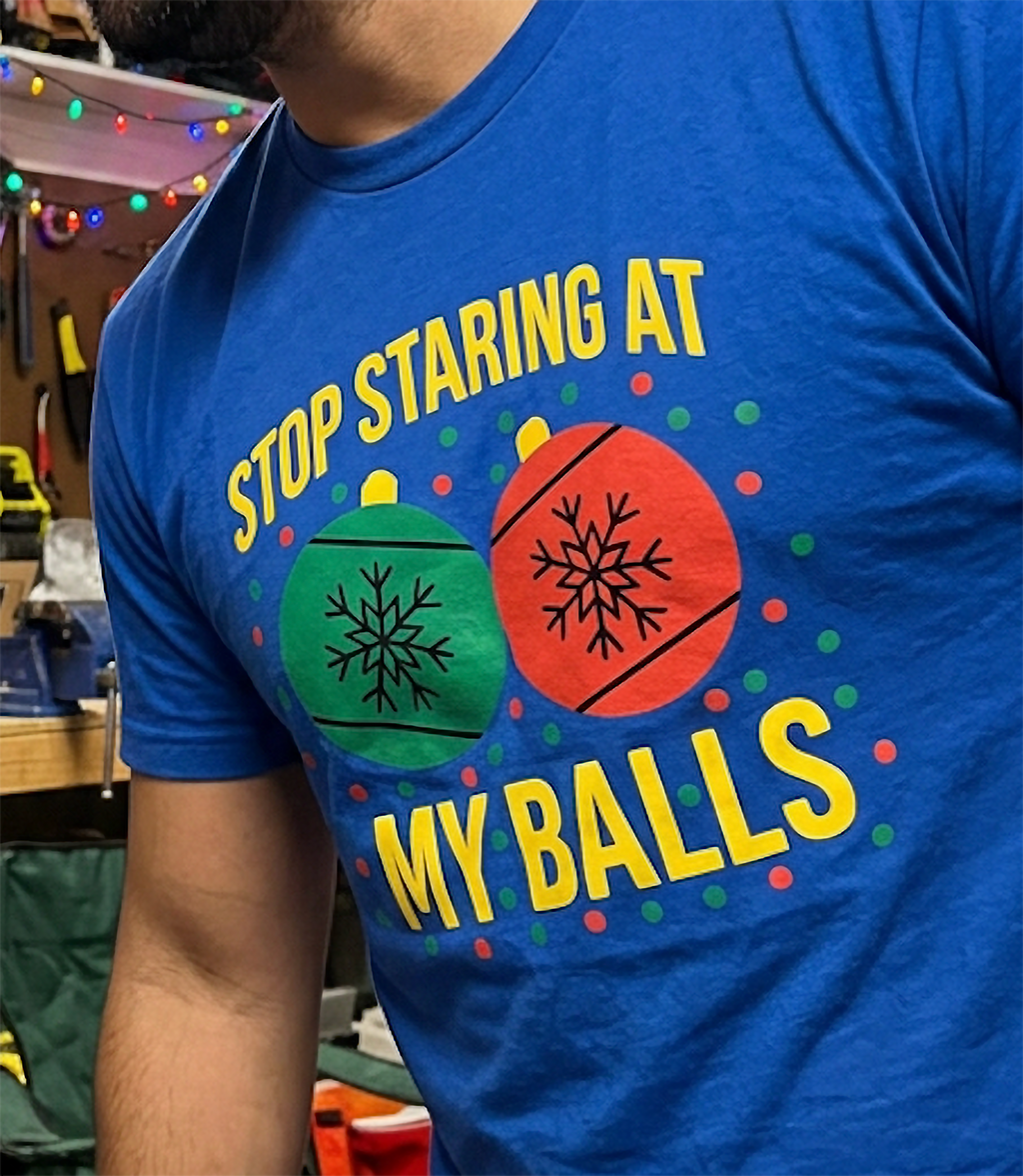 Close-up of blue Christmas ornament t-shirt showing sarcastic Stop Staring at My Balls holiday design.