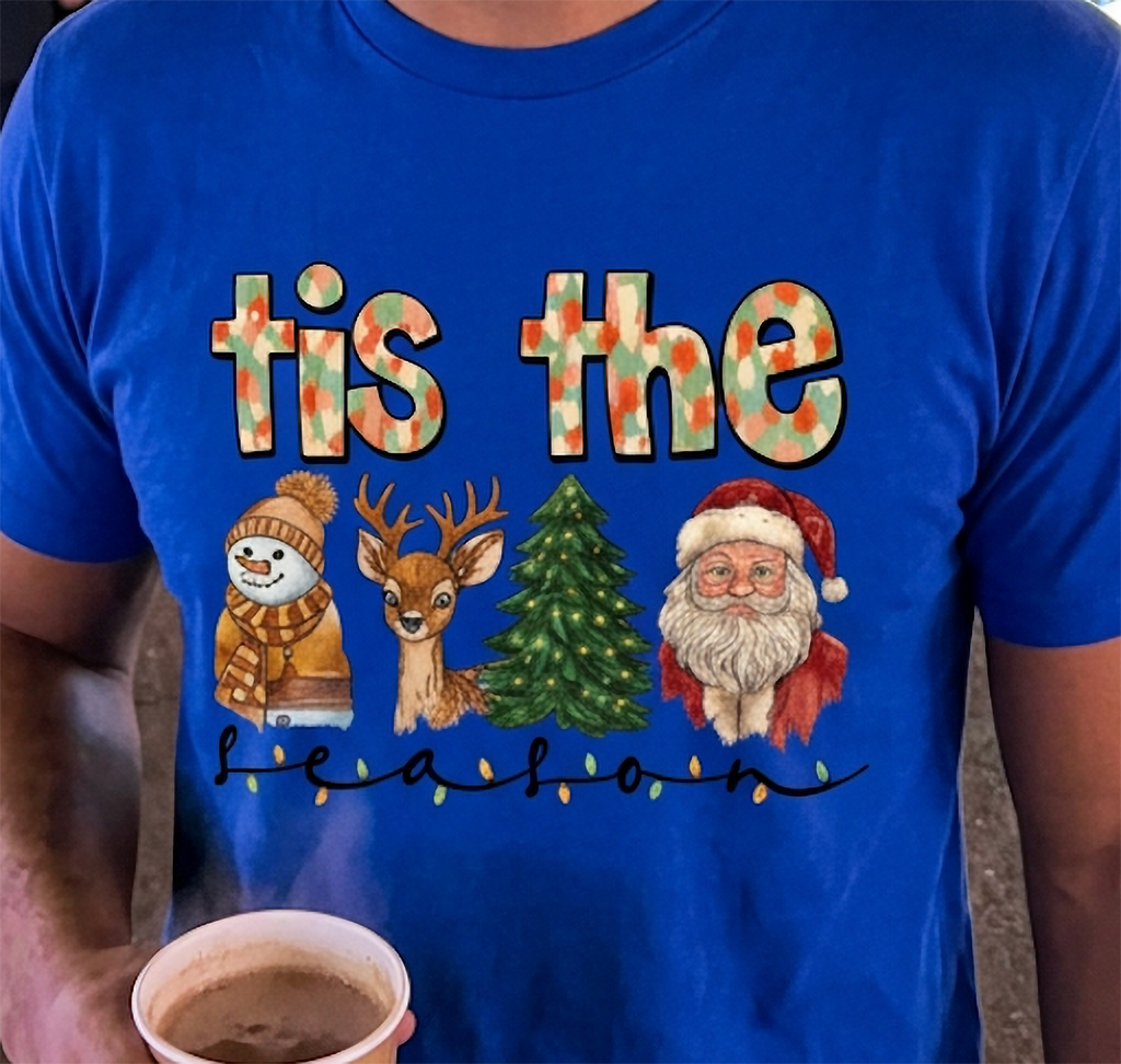 Close-up of blue Tis the Season Christmas t-shirt showing colorful holiday characters, festive lettering, and Christmas light details.