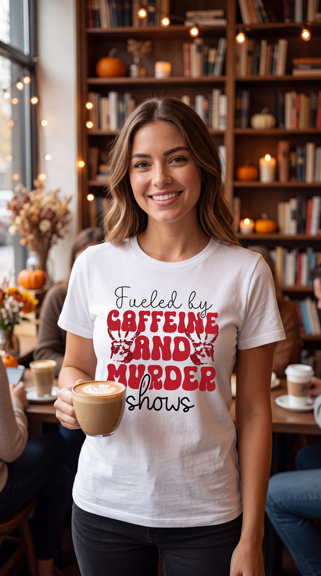 Woman wearing white true crime coffee shirt with Caffeine and Murder Shows graphic while holding coffee in a cafe