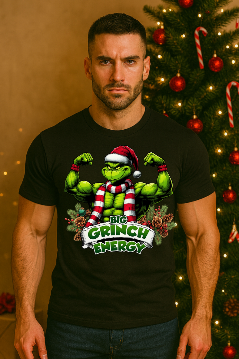 Man wearing a black holiday muscle-energy graphic t-shirt, standing indoors in front of a decorated Christmas tree with festive lights and ornaments.