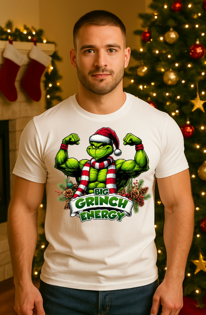 Man wearing a white holiday muscle-energy graphic t-shirt, standing indoors in front of a decorated Christmas tree with warm festive lighting.