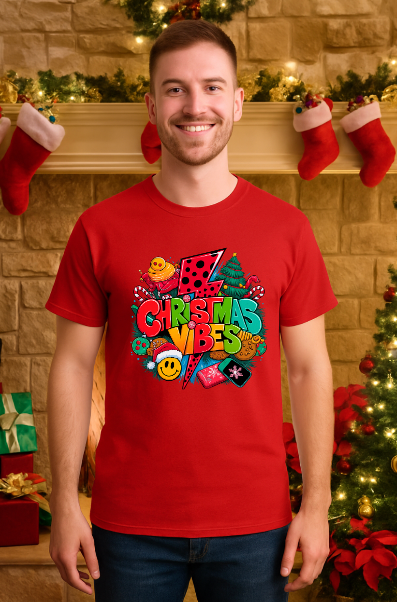 Man wearing a red Christmas Vibes graphic t-shirt with a colorful festive holiday design, standing in a Christmas-themed room with stockings and decorations.