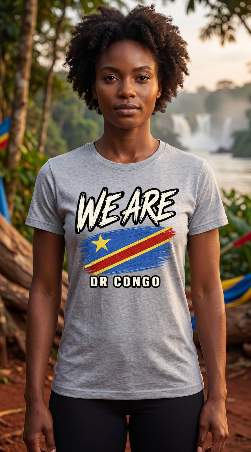 A woman wearing a light gray heather t-shirt with a graphic print of the Democratic Republic of Congo flag and the text 'WE ARE DR CONGO'. The background is a blurred outdoor scene with trees and water.