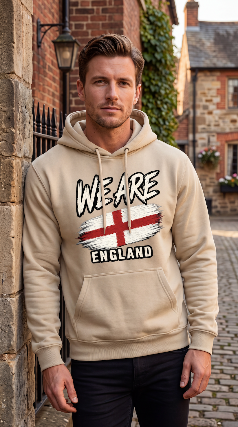 A man wearing a beige hoodie with a graphic print that reads 'WE ARE ENGLAND' above and below a stylized St. George's cross flag, standing outdoors against a stone wall.