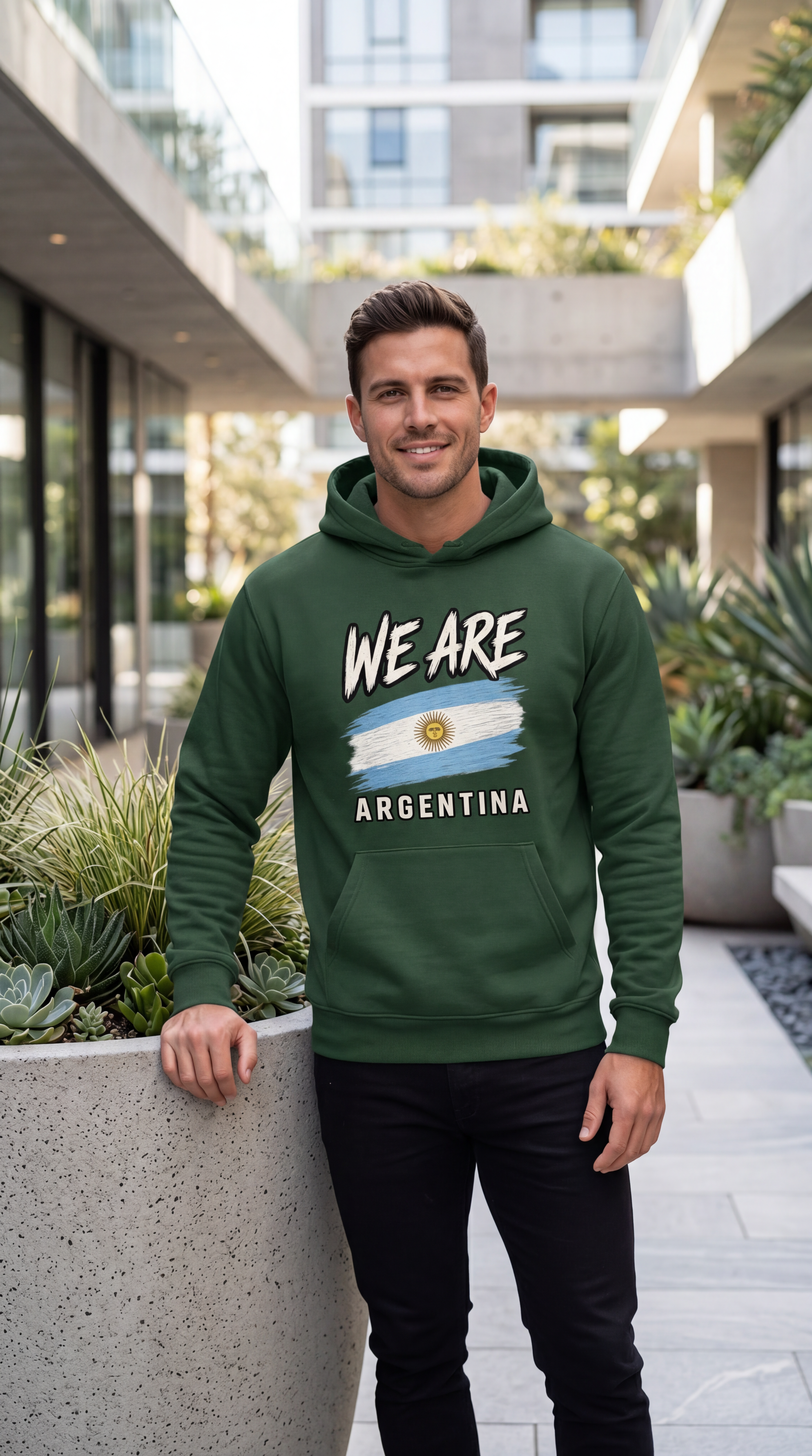 A man wearing a dark green hoodie with a graphic that reads 'WE ARE ARGENTINA' and features the Argentine flag, standing in a modern outdoor walkway.