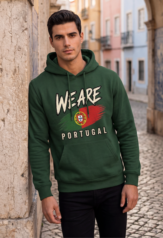 A man wearing a dark green pullover hoodie with a 'WE ARE PORTUGAL' graphic featuring the Portuguese flag, standing in a cobblestone street with colorful buildings in the background.