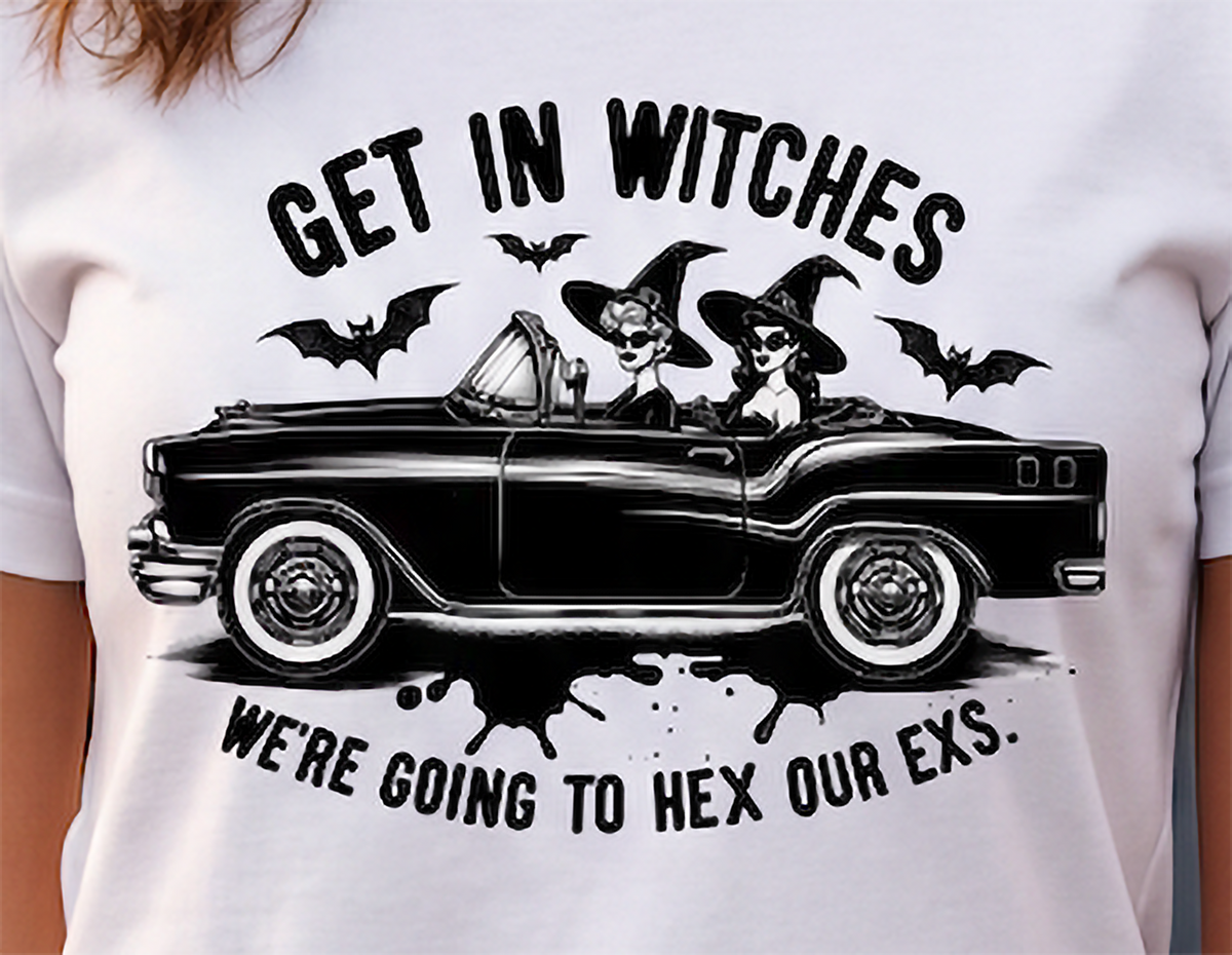 A white short-sleeve graphic t-shirt featuring a black illustration of two witches driving a vintage convertible car, with bats and the text 'GET IN WITCHES WE'RE GOING TO HEX OUR EXS.'.
