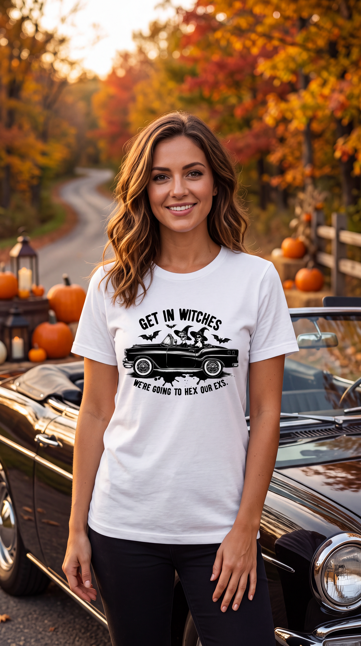 A woman stands outdoors in front of a vintage black car with autumn trees and pumpkins in the background, wearing a white graphic T-shirt that reads 'GET IN WITCHES WE'RE GOING TO HEX OUR EXS.' in black text and illustration.