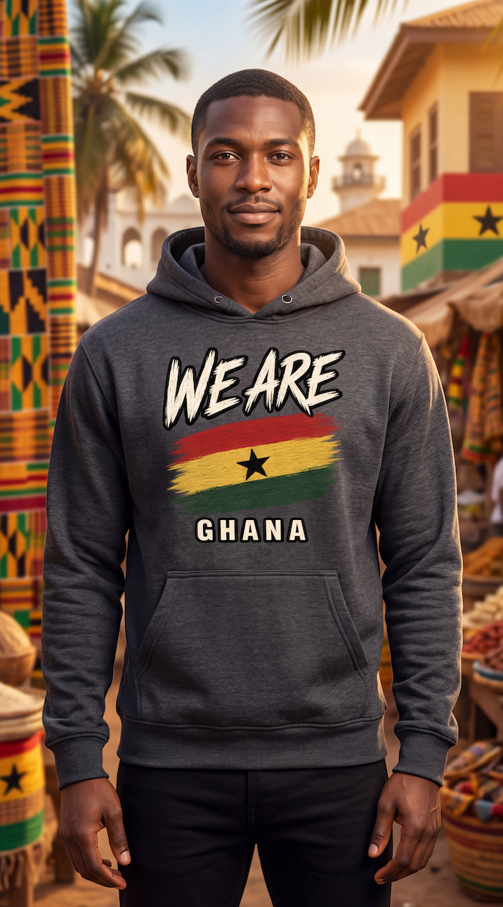 A man wearing a dark gray hoodie with a 'WE ARE GHANA' graphic featuring the Ghana flag, standing in a vibrant outdoor market scene with Ghanaian architecture and textiles in the background.