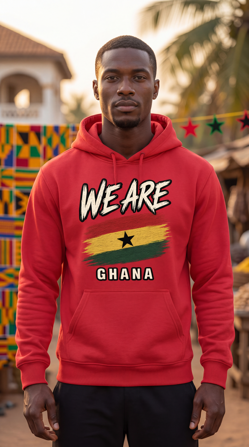 A man wearing a bright red hoodie with a graphic print that reads 'WE ARE GHANA' and features the Ghana flag design, standing outdoors in front of a warm-toned, blurred background.