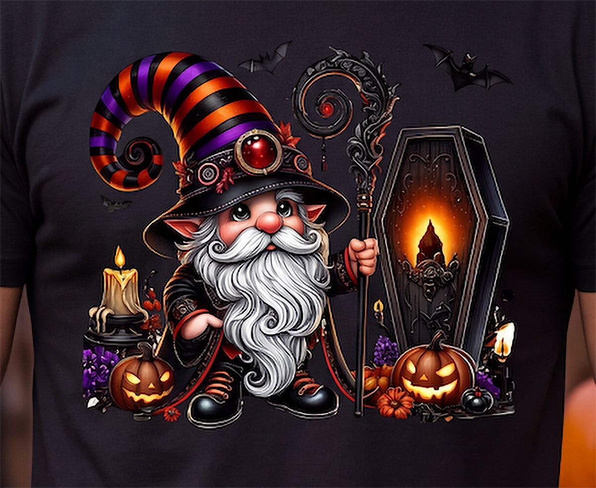 A close-up of a black T-shirt featuring a large, colorful graphic print of a whimsical Halloween gnome. The gnome has a long white beard, a tall striped hat in orange, purple, and black, and holds a staff next to a coffin, pumpkins, candles, and bats.