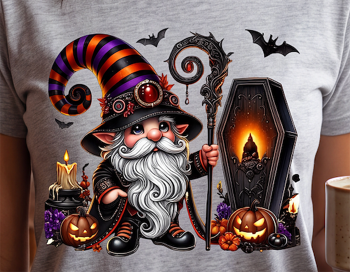 A close-up of a person wearing a light heather gray t-shirt with a large, colorful graphic print of a cute cartoon wizard holding a coffin and staff, surrounded by pumpkins, candles, and bats.