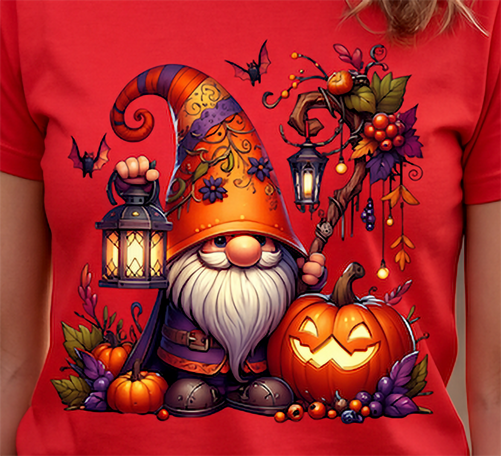A red short-sleeve T-shirt worn by a person, featuring a large colorful Halloween gnome graphic on the front. The design includes a tall orange hat, white beard, lantern, pumpkins, bats, and autumn leaves.