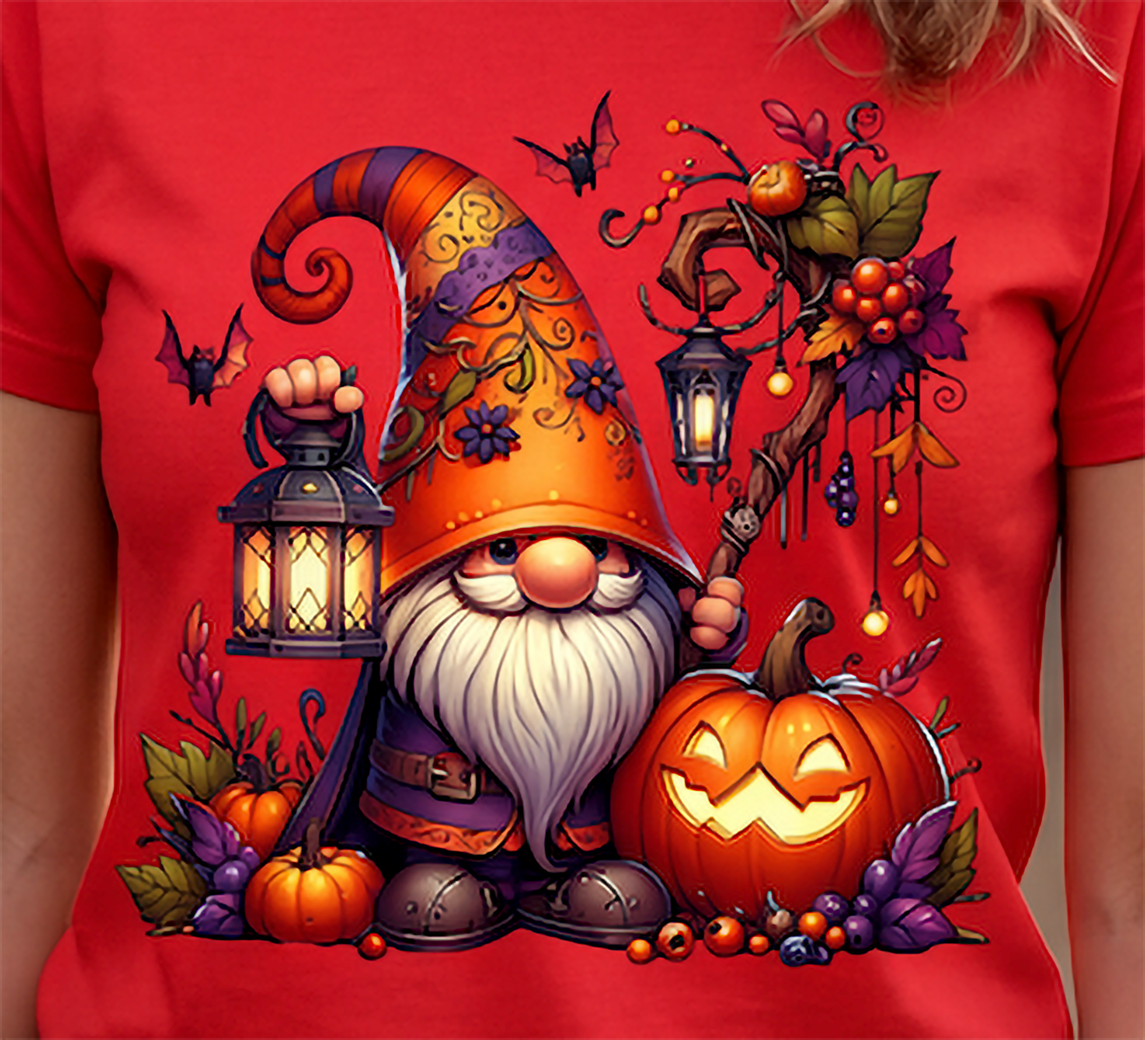 A red short-sleeve T-shirt worn by a person, featuring a large colorful Halloween gnome graphic on the front. The design includes a tall orange hat, white beard, lantern, pumpkins, bats, and autumn leaves.