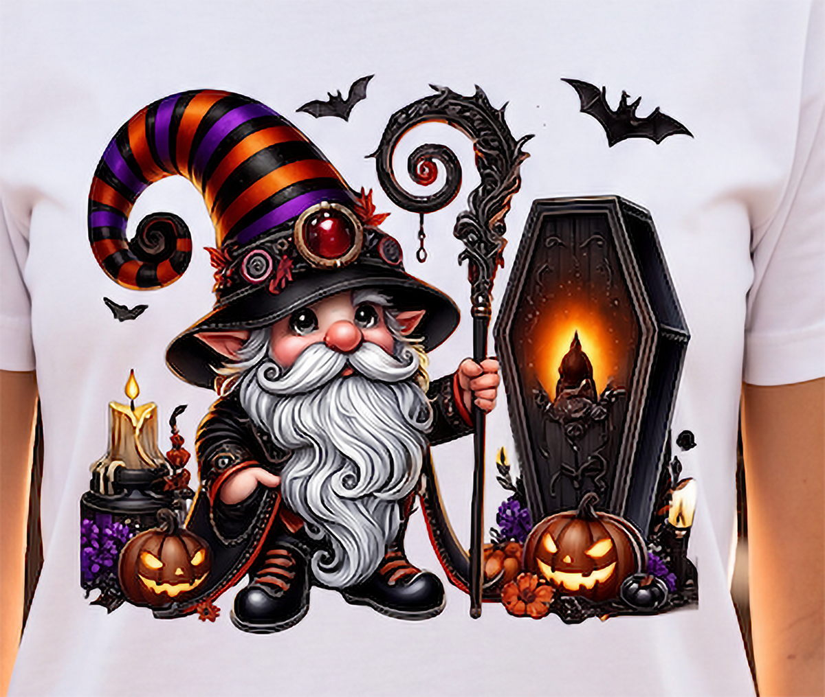 A close-up of a white T-shirt featuring a large, colorful graphic print of a cartoon witch with a striped hat, long white beard, and staff, standing next to a glowing coffin with pumpkins and bats around it.