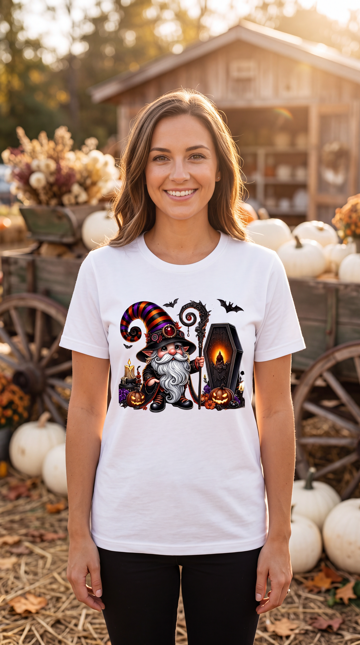 A woman wearing a white graphic t-shirt with a Halloween gnome design, standing in an outdoor autumn market setting with pumpkins and lanterns.