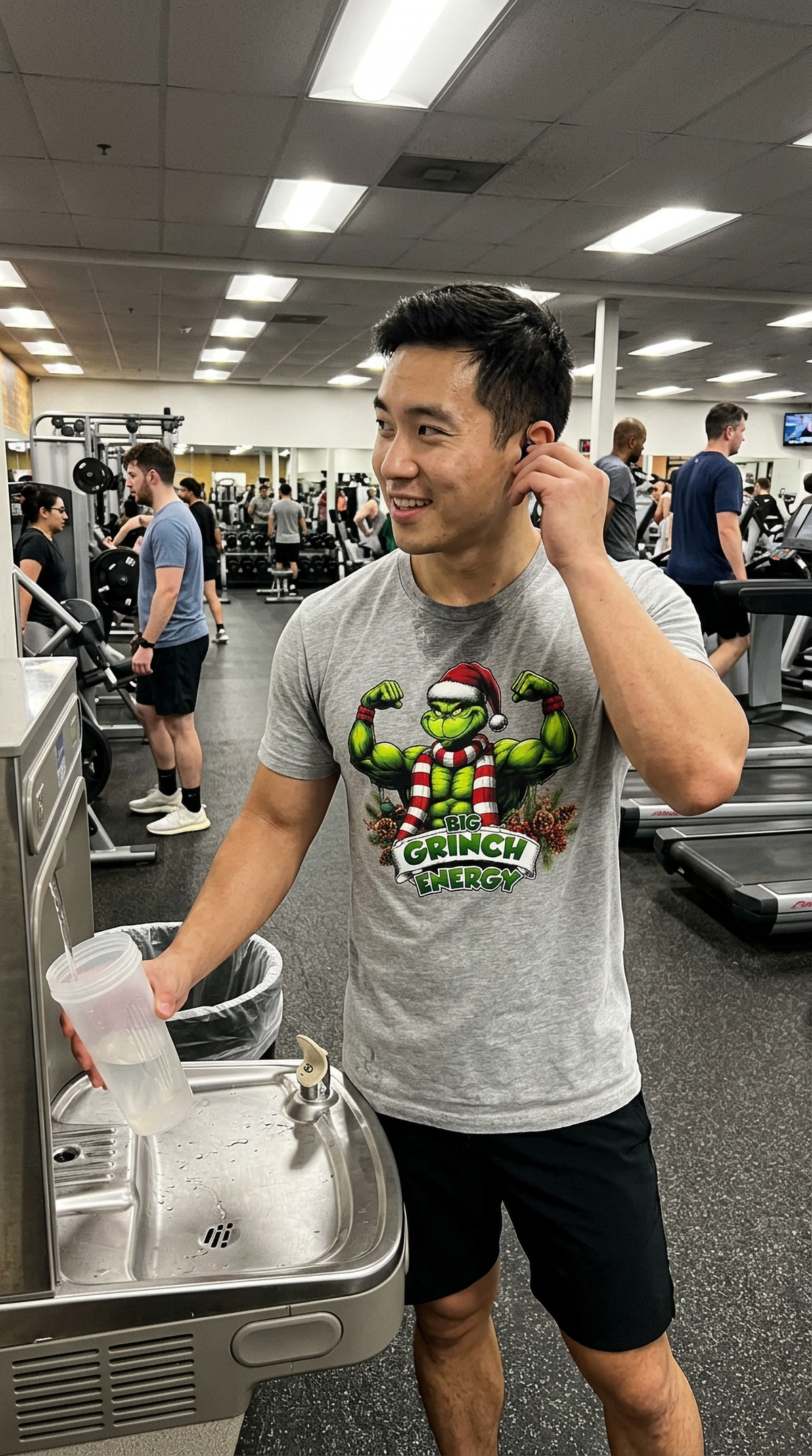 Man wearing heather gray Big Grinch Energy Christmas t-shirt at the gym featuring a funny muscular Grinch holiday design.