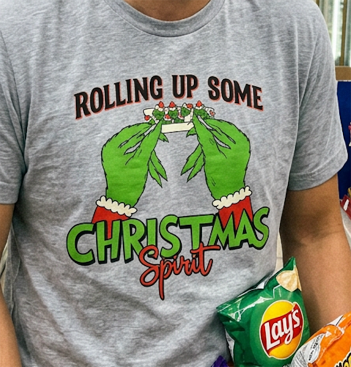 Close-up of heather gray weed Christmas shirt showing festive green hands and bold red and green holiday typography.