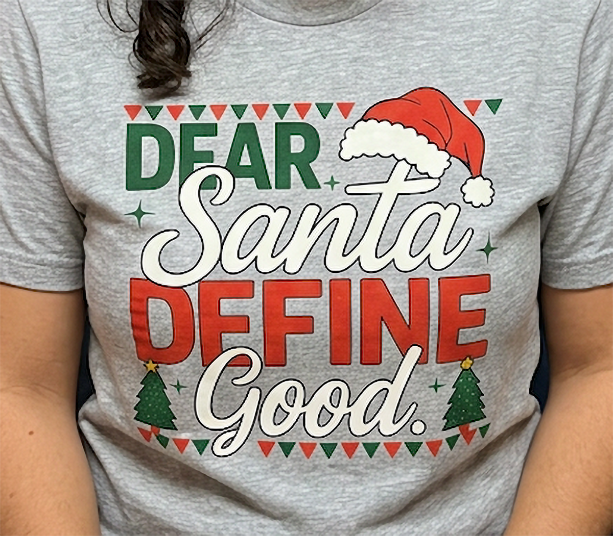 Heather Gray Close-Up: Close-up of the Dear Santa Define Good Christmas graphic on heather gray fabric with holiday lettering and Santa hat.