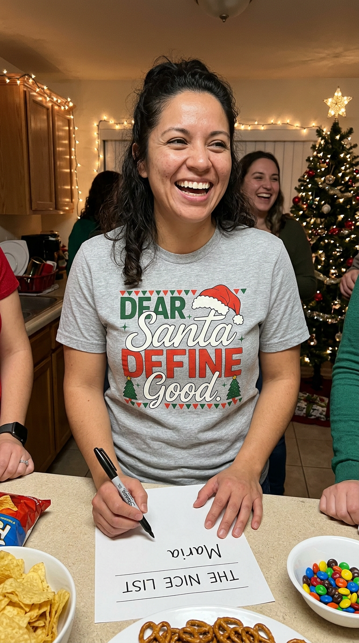 Lifestyle – Heather Gray: Woman wearing a heather gray Dear Santa Define Good Christmas graphic t-shirt in a festive kitchen setting.