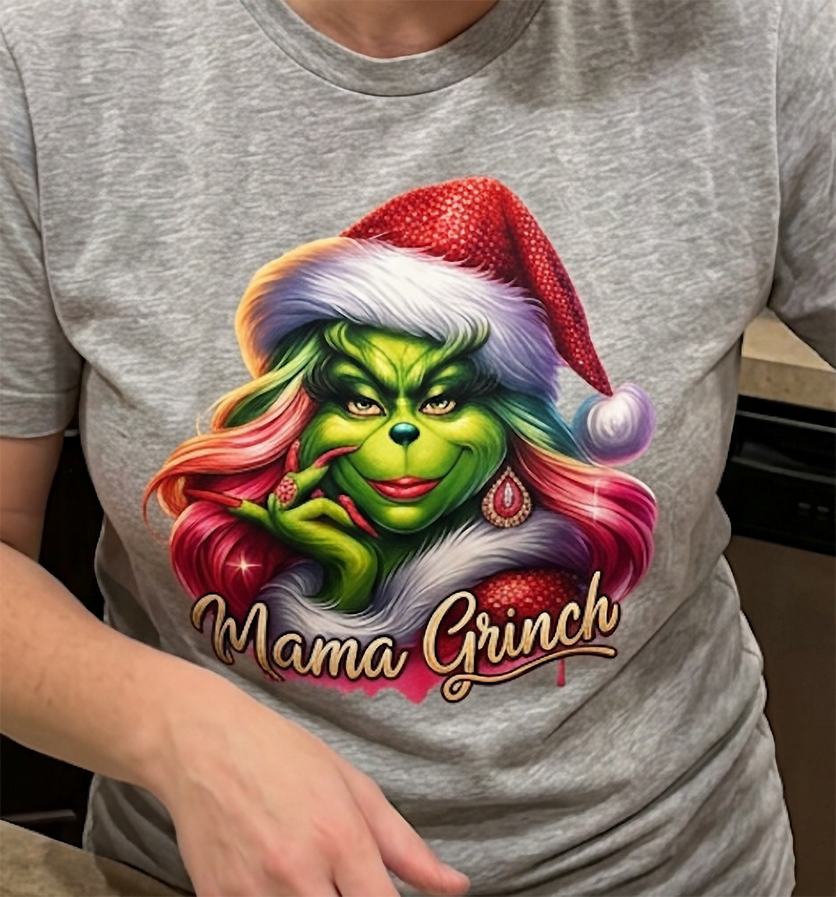 Close-up of heather gray Mama Grinch Christmas shirt showing colorful holiday graphic and festive pink hairstyle.
