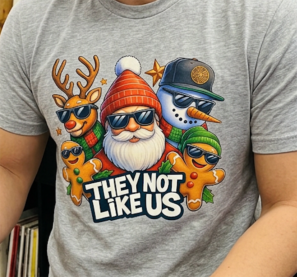 Close-up of heather gray They Not Like Us Christmas shirt featuring colorful holiday characters wearing sunglasses.