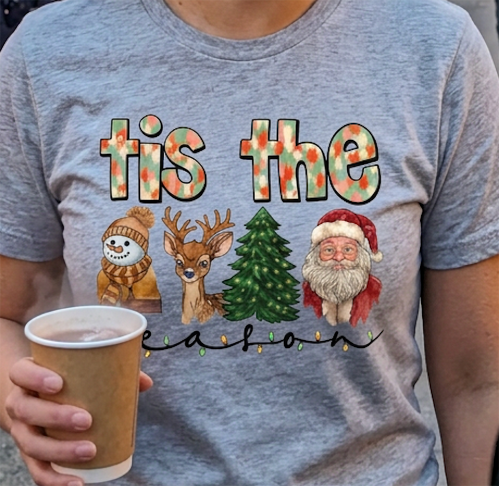 Close-up of heather gray Tis the Season Christmas t-shirt showing detailed holiday character artwork and colorful festive typography.