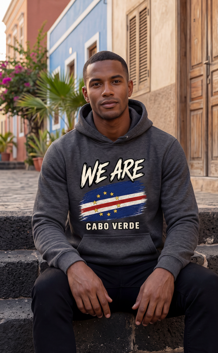 A man sitting on stone steps wearing a dark gray hoodie with a Cabo Verde flag graphic and the text 'WE ARE CABO VERDE'.