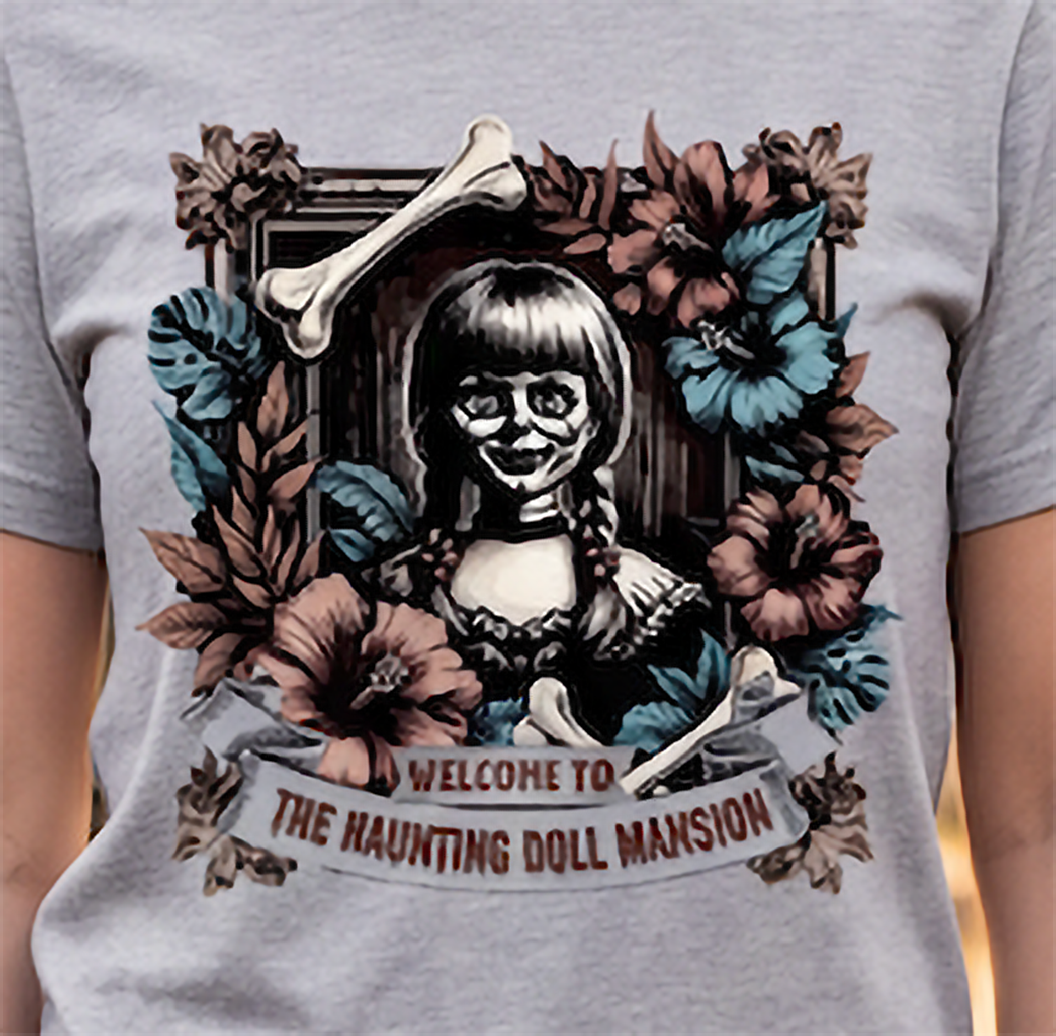 Close-up of creepy doll Halloween graphic on heather gray shirt with dark floral mansion design