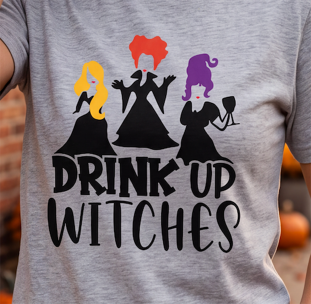 Close-up of heather gray Drink Up Witches Halloween shirt with colorful witch design