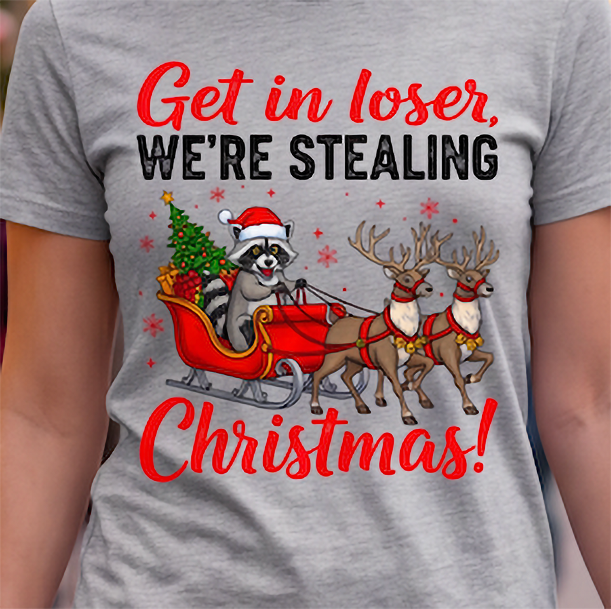 Close-up of Get in Loser We’re Stealing Christmas raccoon graphic printed on a heather gray T-shirt.