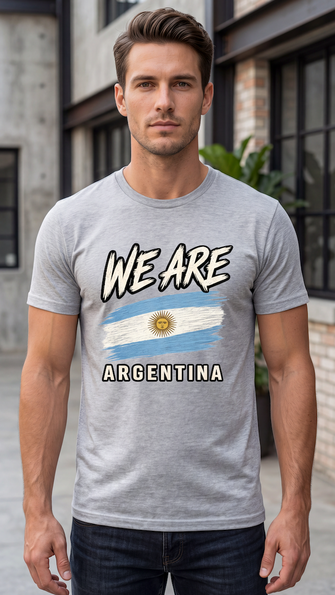 A man wearing a heather gray t-shirt with a graphic that reads 'WE ARE ARGENTINA' above and below an Argentina flag design, standing in front of a blurred building background.