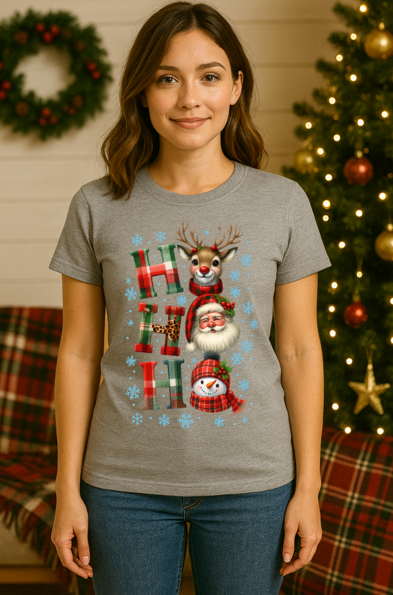 Woman wearing a gray Ho Ho Ho Christmas t-shirt with Santa, reindeer, and snowman graphic in a festive holiday living room setting.