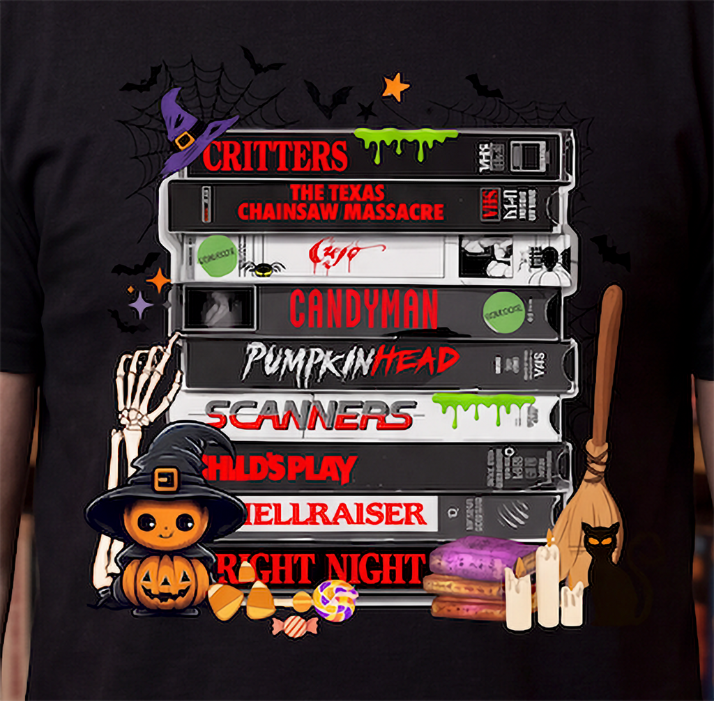 A black short-sleeve T-shirt with a large colorful graphic print on the front. The graphic shows a stack of VHS tapes with horror movie titles including 'Critters', 'The Texas Chainsaw Massacre', 'Candyman', 'Pumpkinhead', 'Scanners', 'Wild Play', 'Telriser', and 'Right Night', surrounded by Halloween elements like a witch hat, skeleton hand, broom, candy, and a jack-o'-lantern.