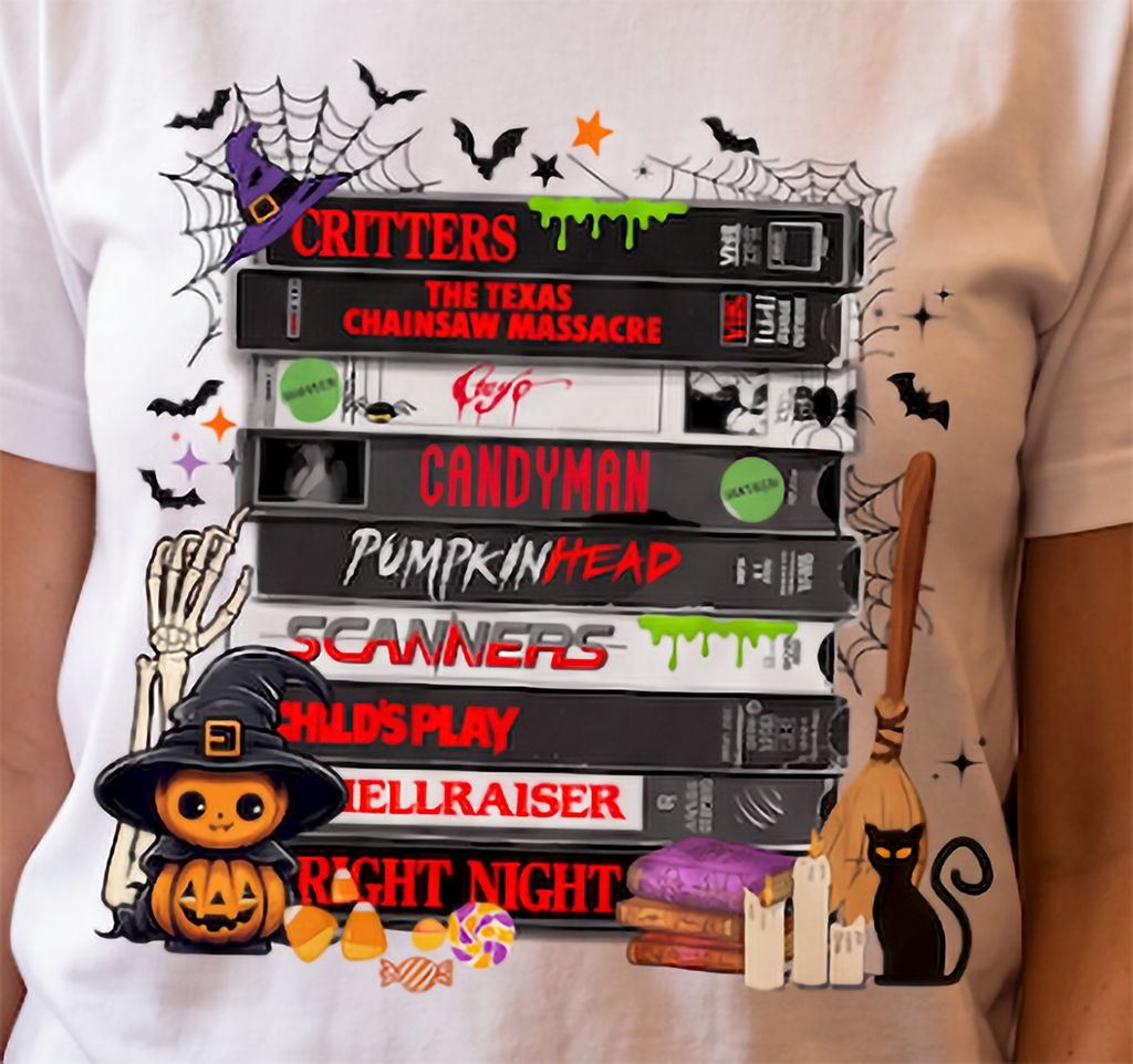Close-up of horror movie VHS graphic on white T-shirt with retro scary movie tapes, Halloween spiderwebs, bats, pumpkin and black cat.