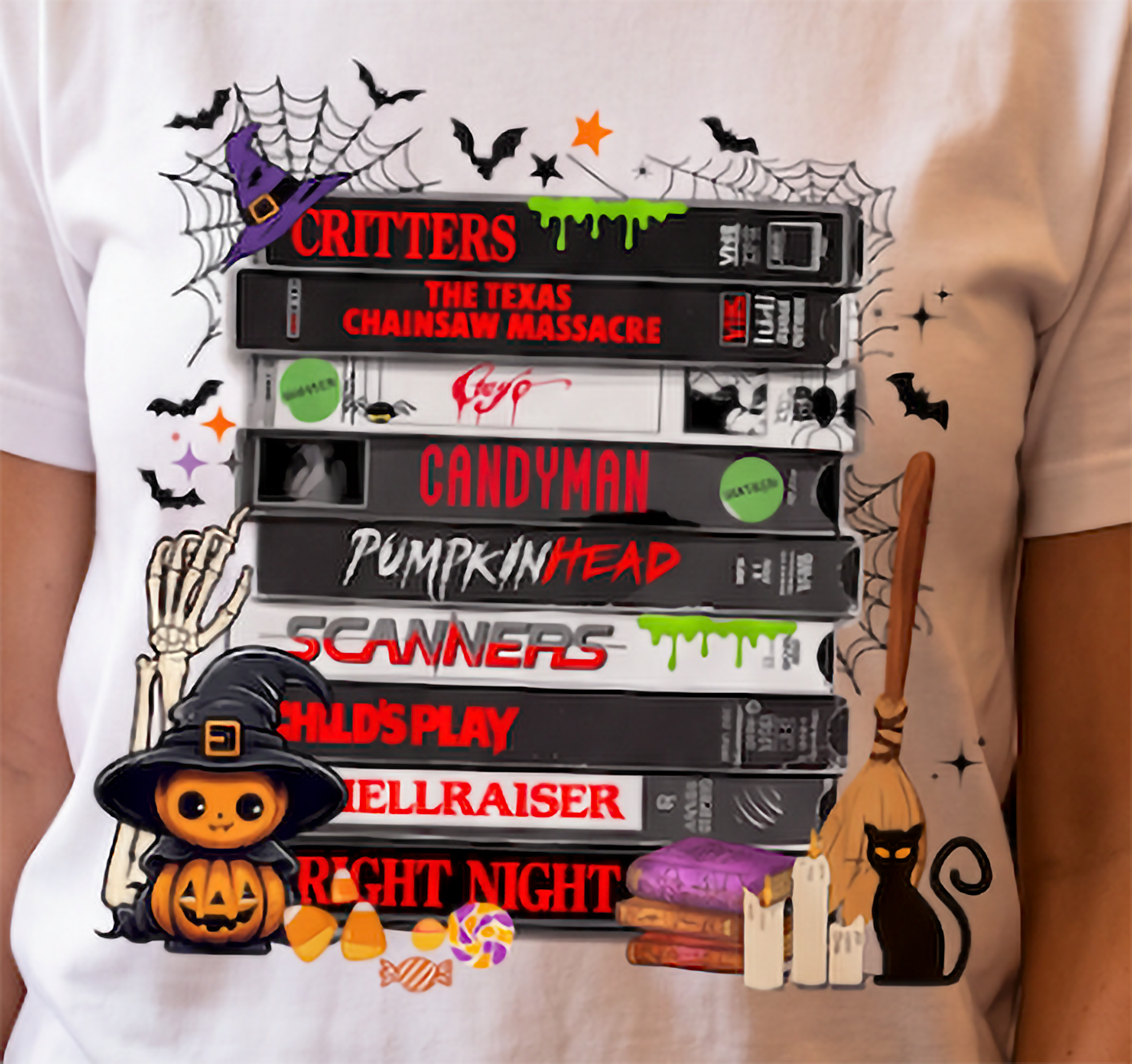 Close-up of horror movie VHS graphic on white T-shirt with retro scary movie tapes, Halloween spiderwebs, bats, pumpkin and black cat.