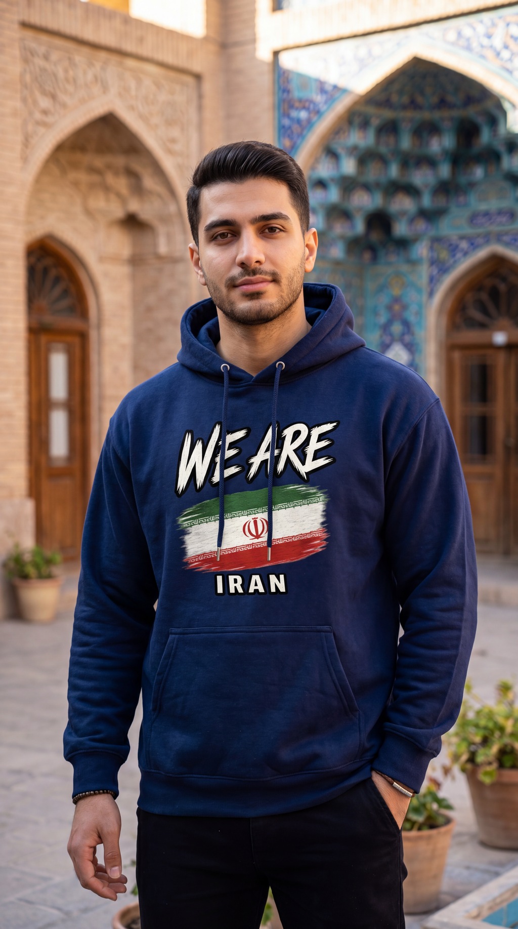 A man wearing a navy blue hoodie with a graphic print that reads 'WE ARE' above an Iranian flag design and 'IRAN' below, standing in front of an ornate architectural background with arches and columns.