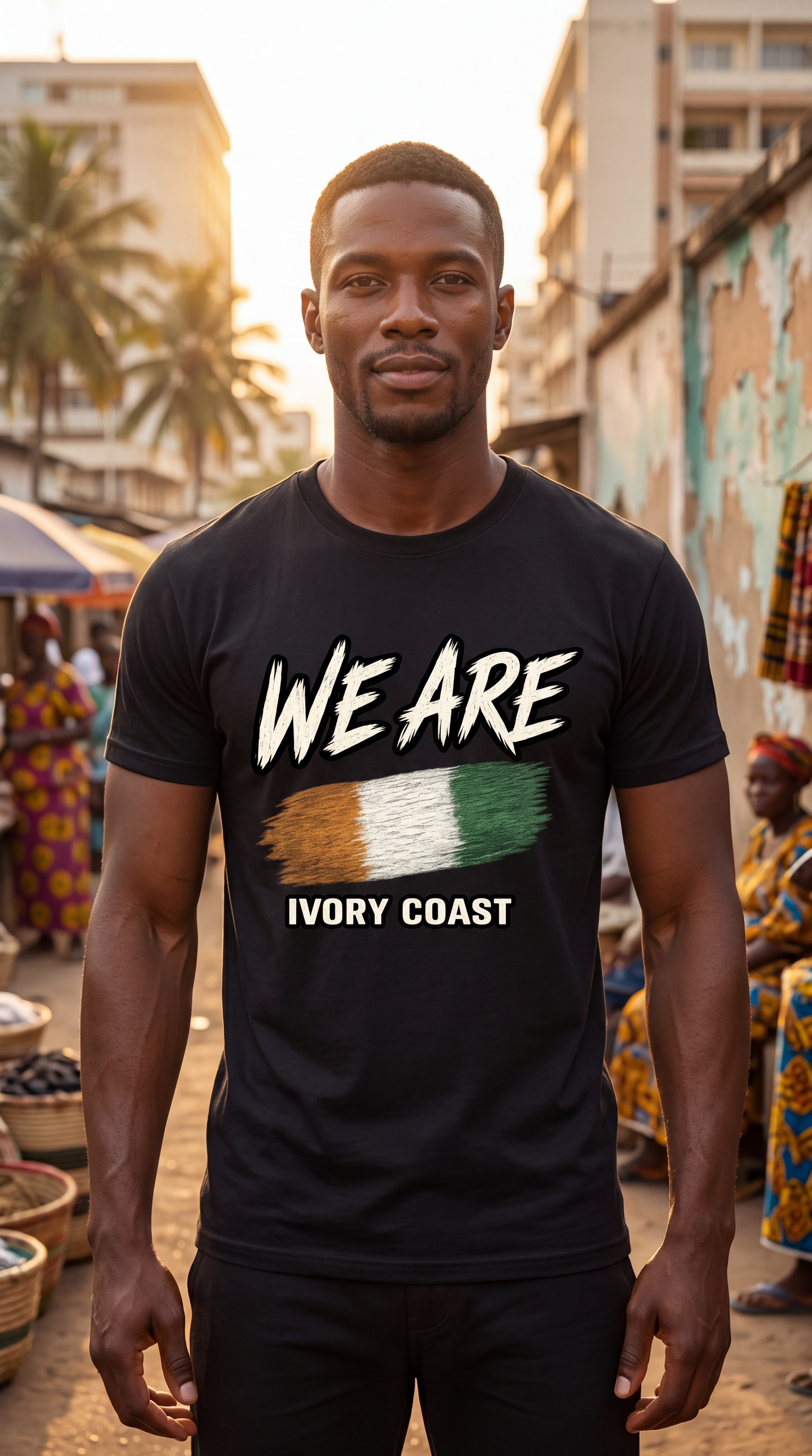 A man wearing a black t-shirt with a graphic that reads 'WE ARE' above the Ivory Coast flag and 'IVORY COAST' below, standing in an outdoor market setting.