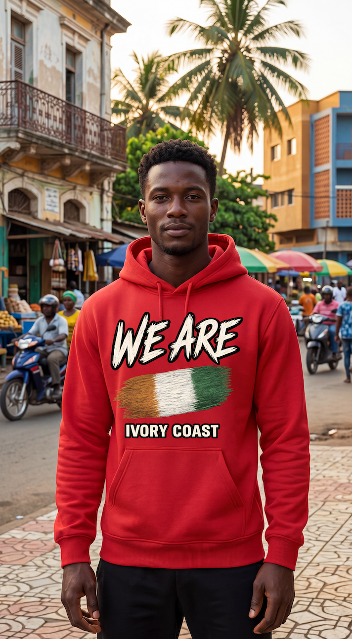 A man wearing a red hoodie with a graphic print that reads 'WE ARE' above an Ivory Coast flag and 'IVORY COAST' below, standing in a busy outdoor street scene.