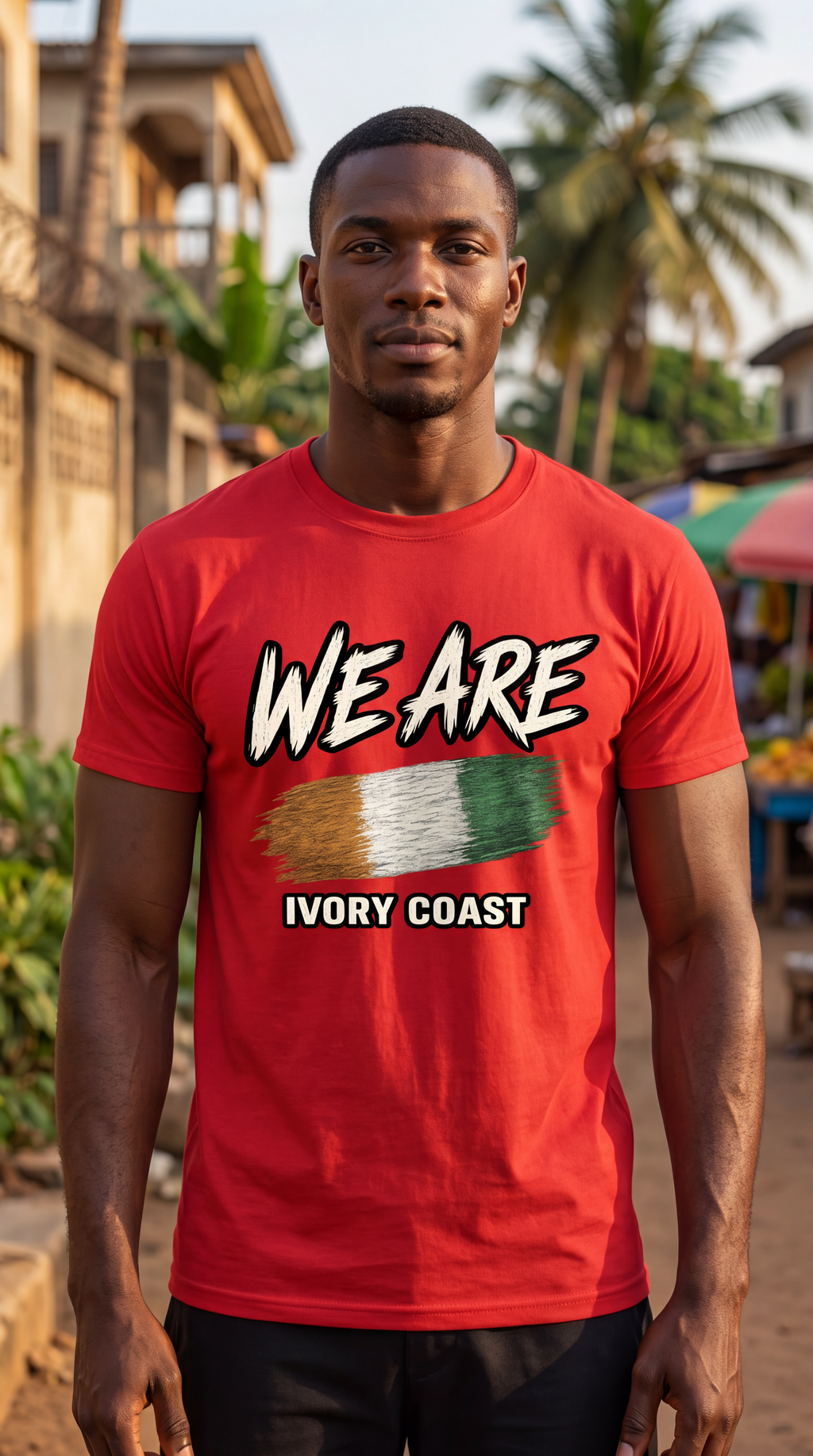 A man wearing a red graphic t-shirt with 'WE ARE IVORY COAST' and a stylized Ivory Coast flag design, set against a blurred outdoor street background.