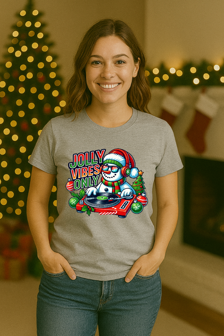 Woman wearing a gray Bella+Canvas 3001 Christmas t-shirt with a DJ snowman graphic and “Jolly Vibes Only” text, styled in a festive holiday setting