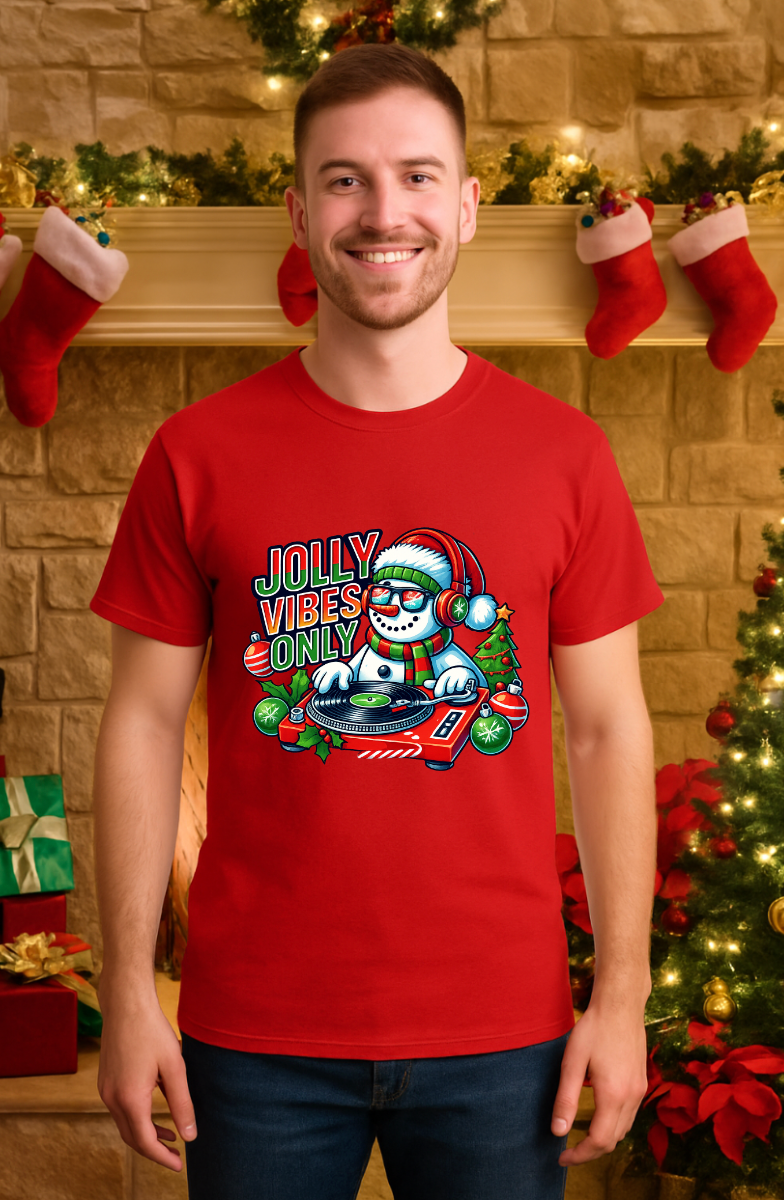 Man wearing a red Bella+Canvas 3001 Christmas t-shirt with a DJ snowman graphic and “Jolly Vibes Only” text, styled in a festive holiday living room setting