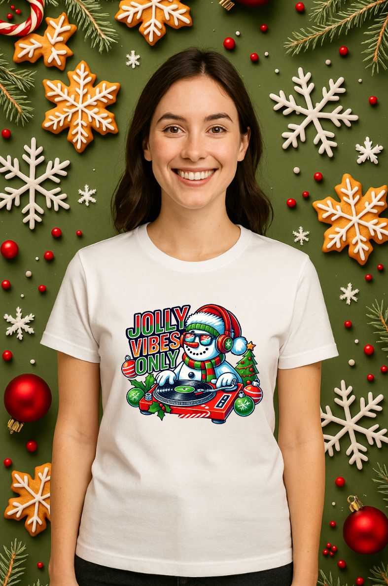 Woman wearing a white Bella+Canvas 3001 Christmas t-shirt with a DJ snowman graphic and “Jolly Vibes Only” text, styled with festive holiday decorations