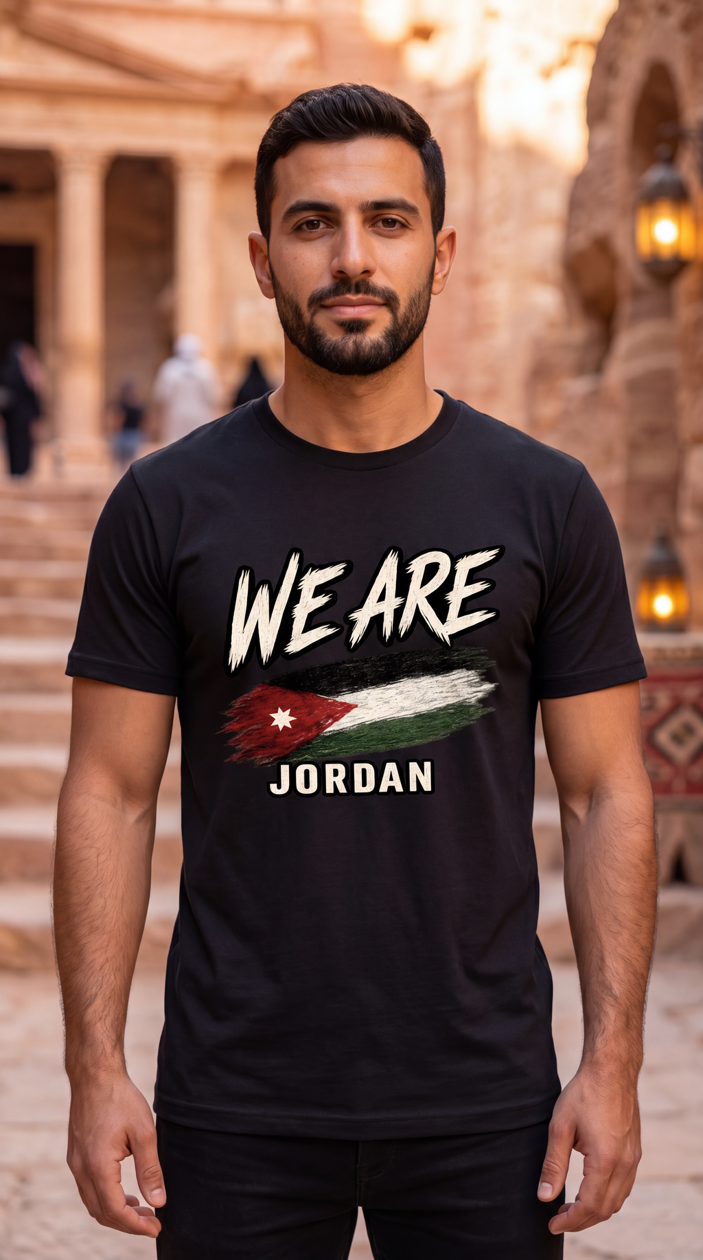 A man wearing a black graphic t-shirt with 'WE ARE JORDAN' and a stylized Jordan flag design, standing in front of a warm, blurred stone architectural background.