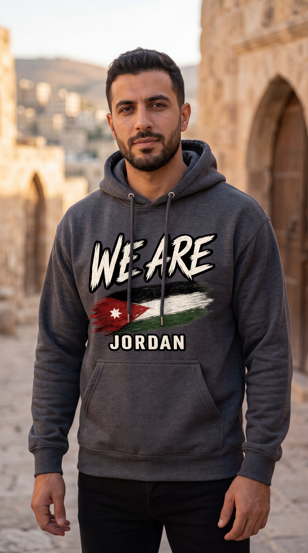 A man wearing a dark gray hoodie with a graphic print that reads 'WE ARE JORDAN' and features the Jordan flag, standing in an outdoor stone-walled environment.