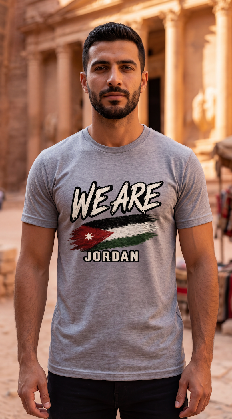 A man wearing a heather gray graphic t-shirt with 'WE ARE JORDAN' and a stylized Jordan flag design, standing in front of a warm, sandy stone background.