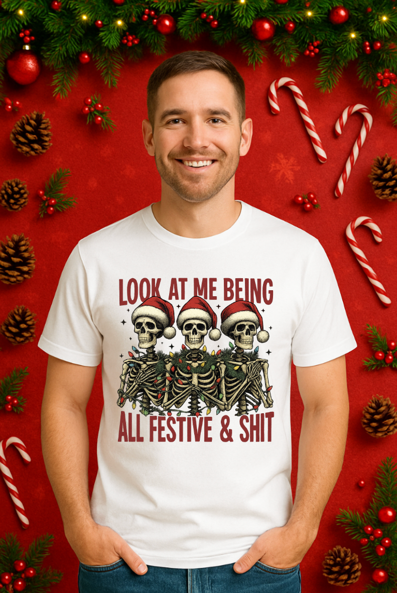 Man wearing a white Christmas skeleton shirt featuring three skeletons in Santa hats with the text “Look At Me Being All Festive & Shit,” shown on a festive red holiday background