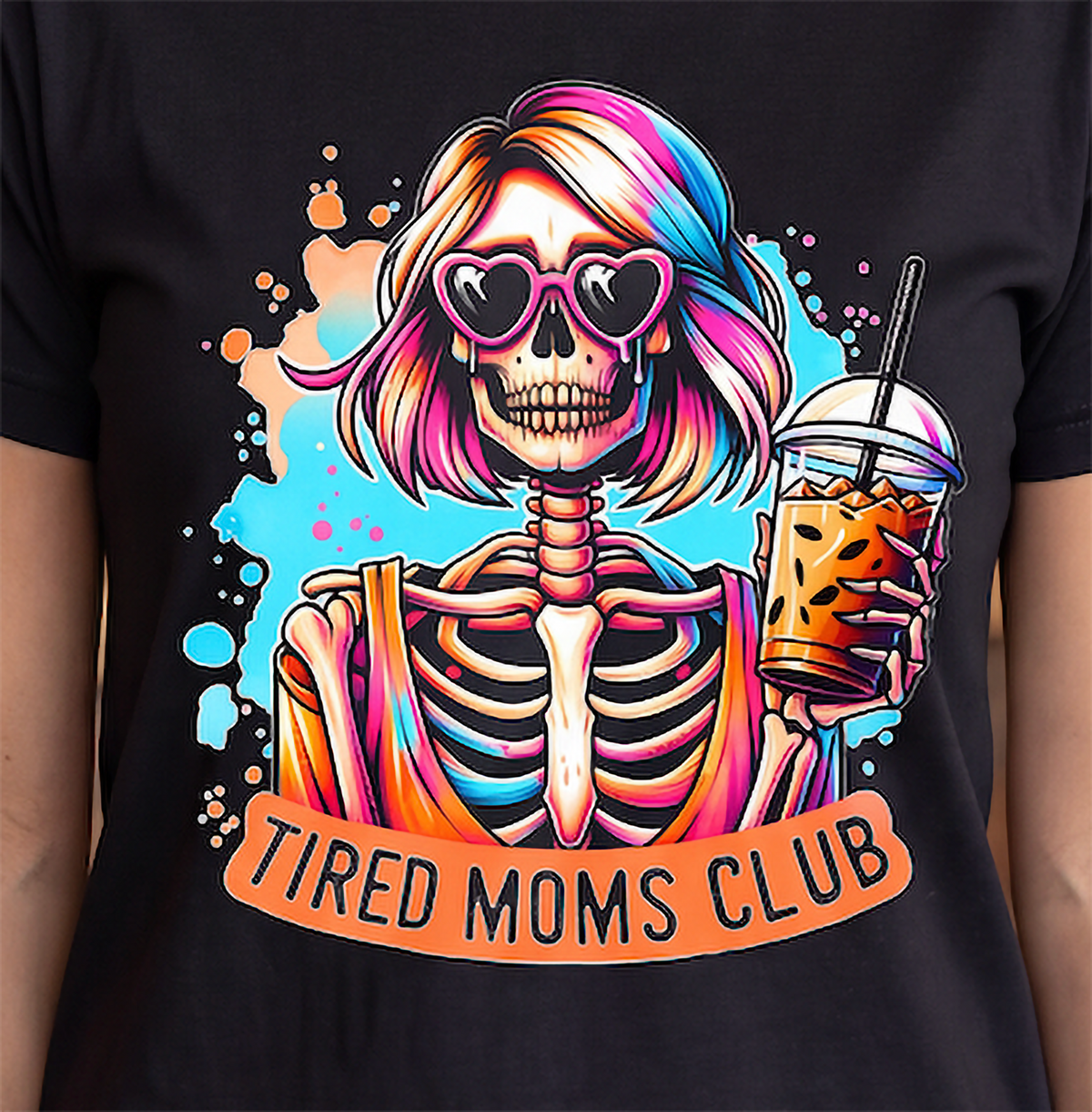 A black short-sleeve T-shirt featuring a colorful graphic of a skeleton woman with pink and blue hair, heart-shaped sunglasses, and an iced coffee, with the text 'TIRED MOMS CLUB' below.