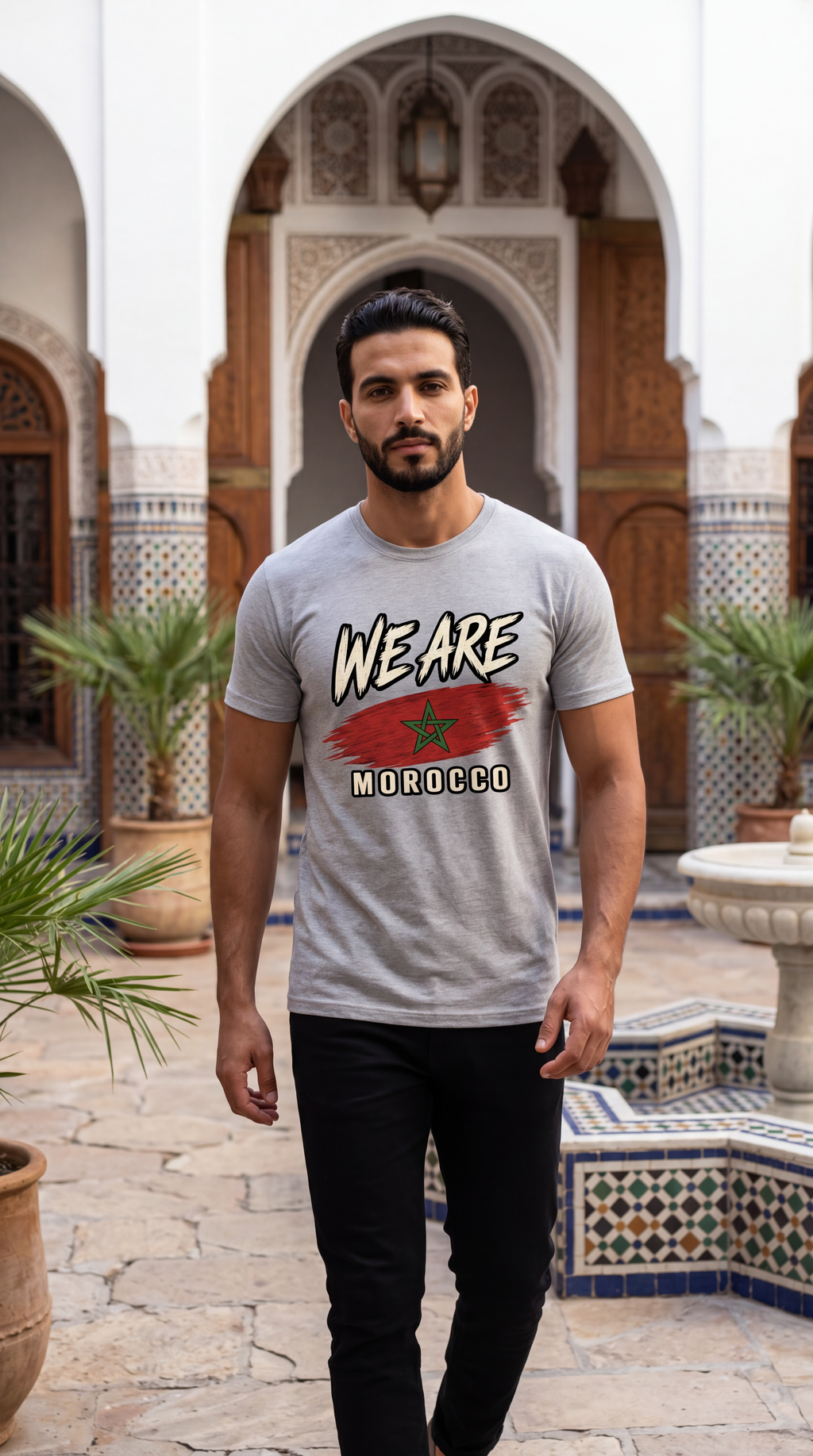 A man wearing a light gray graphic t-shirt with 'WE ARE MOROCCO' and a red star design, standing in a Moroccan courtyard with arches and tiled floors.